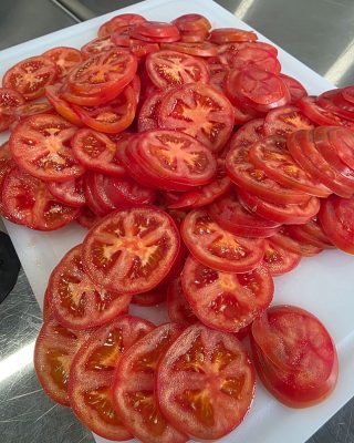 Sliced tomatoes arranged on a white cutting board, ready for preparation or serving.