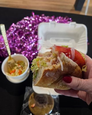 A person holding a sandwich alongside a small bowl of fresh salad.