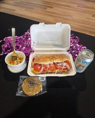 A sandwich, a bag of chips, and a drink placed together in a takeout container.