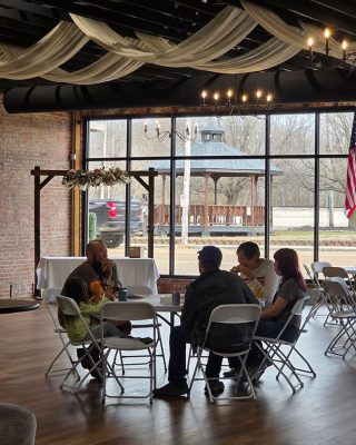 A group of people seated at tables in a well-lit room, engaged in conversation and activities.