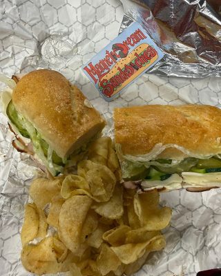 A sandwich with chips and a drink placed on a paper surface, ready for a meal.